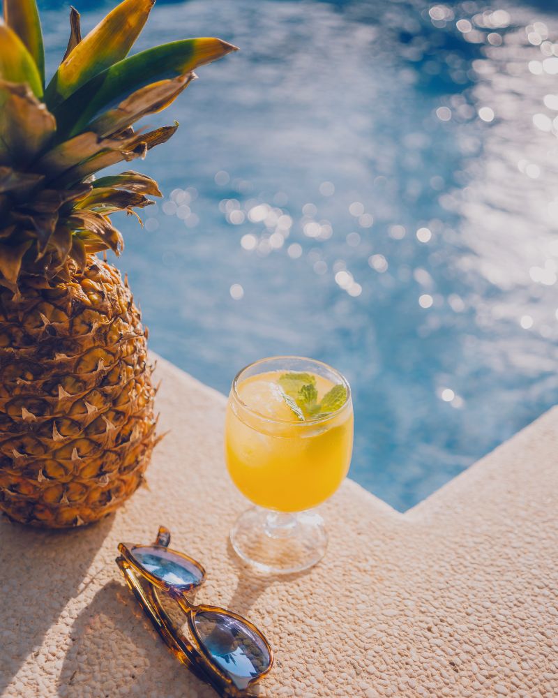 a pineapple next to a drink and sunglasses