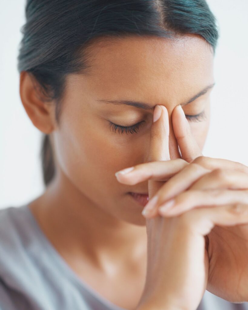 a woman holding her eyes closed, stressed and tired after a night of revenge bedtime procrastination