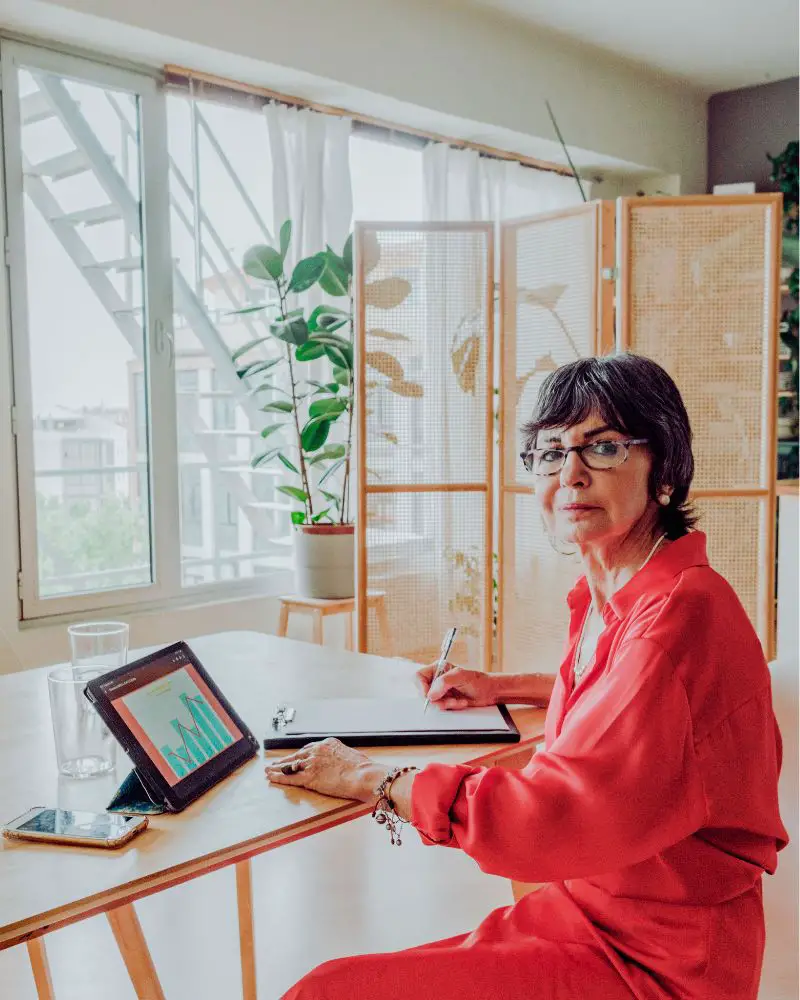 a woman sitting at a table with a tablet and a screen