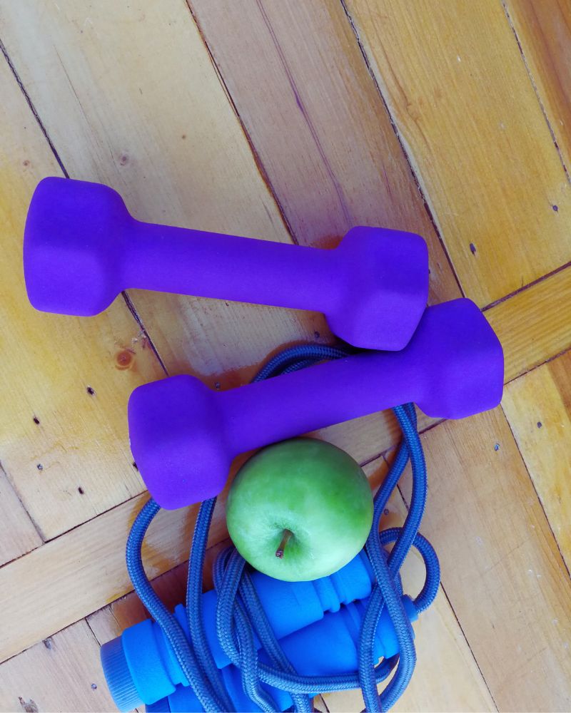 a pair of purple dumbbells and a green apple on a wooden floor to demonstrate the best exercise equipment over 60