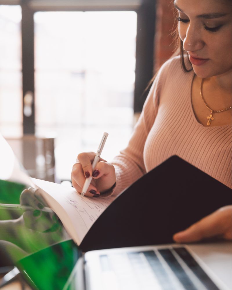 a woman writing in a notebook using an executive function planner for adults