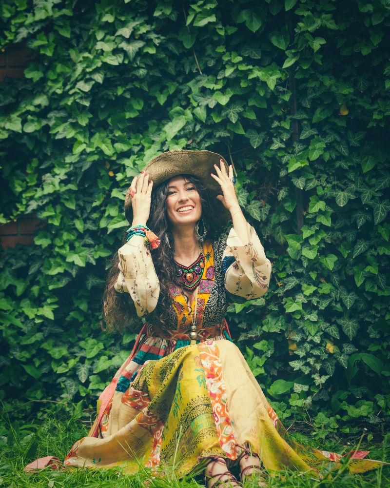 a woman in a hat sitting on grass wearing boho style over 50